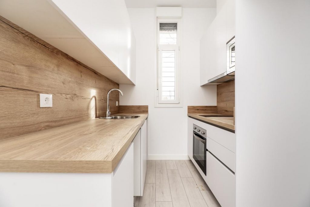 Newly installed small kitchen with plain white cabinets, light wood countertops with matching backsplashes and a narrow window